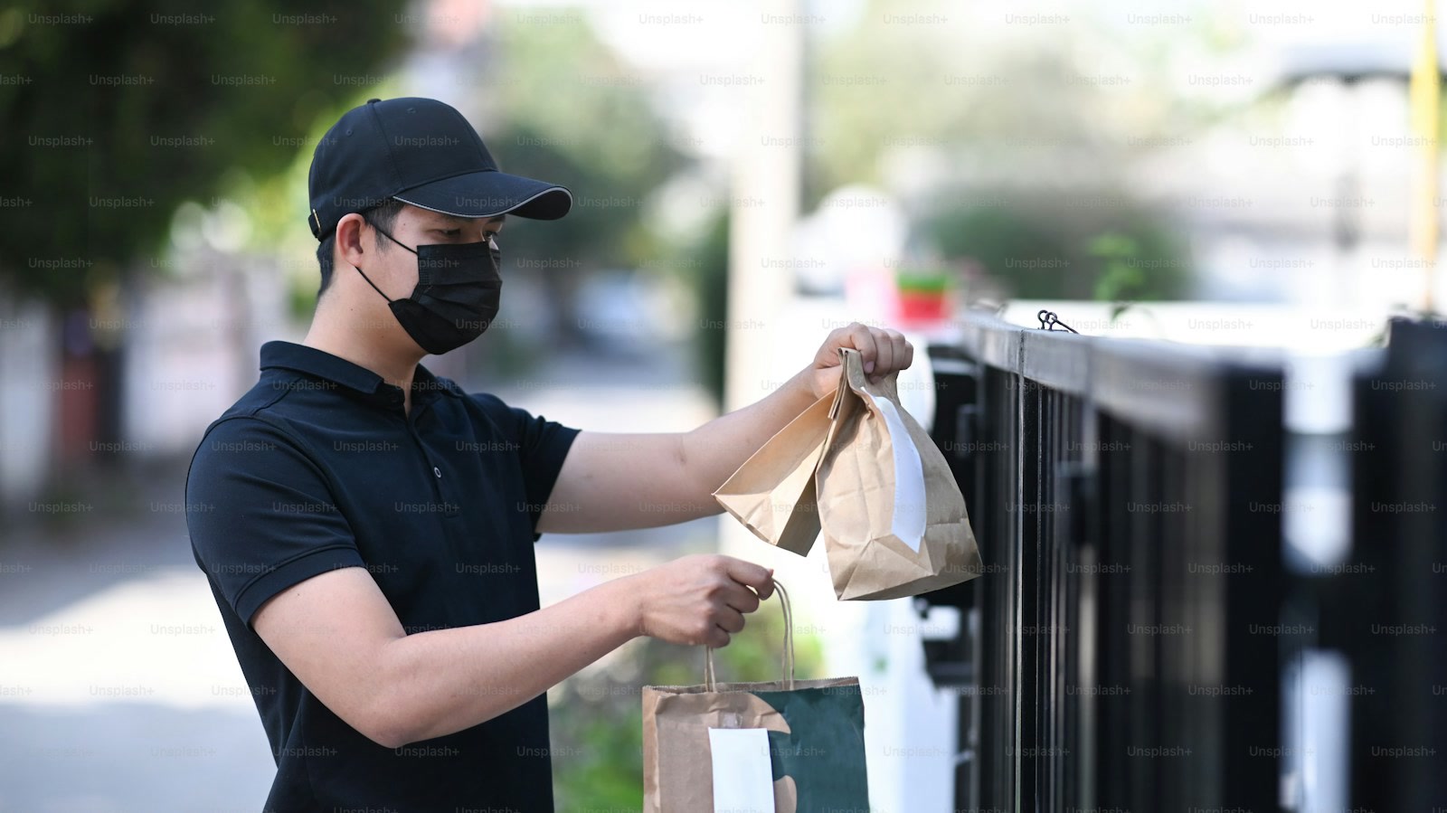 Food delivery courier placing brown takeaway bags on a residential gate